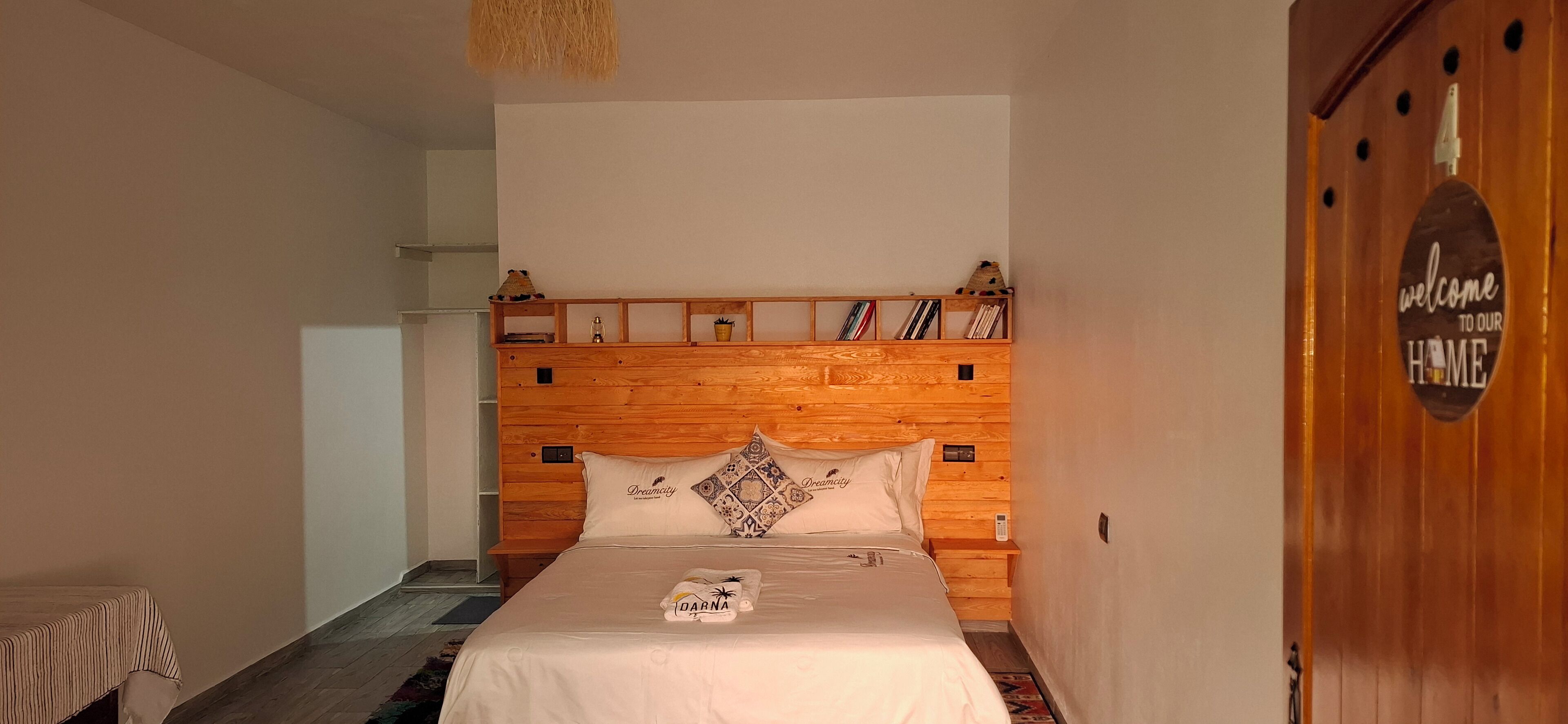 Een slaapkamer met een houten hoofdeinde, een bed met witte beddengoed en een welkomstbordje op de deur.