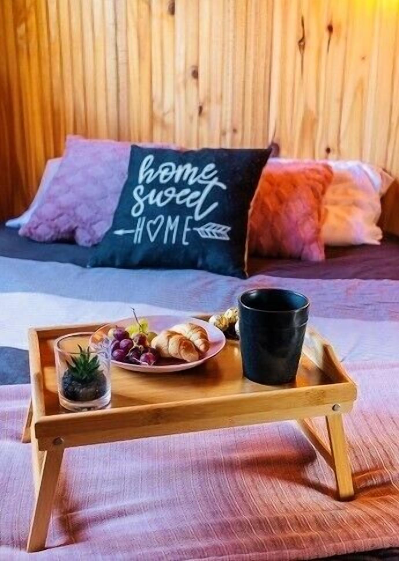 A wooden bed with a pillow that reads "home sweet home" and a tray with food and a drink.