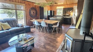 Un salon confortable avec un canapé, une table basse en verre, une table à manger avec des chaises, une cuisine équipée d’une cuisinière et une grande fenêtre donnant sur un paysage naturel.