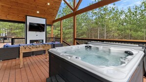 A wooden deck with a hot tub, outdoor seating, and a TV screen. - Couples - Family - Games - Hot tub - Sauna (Broken Bow)