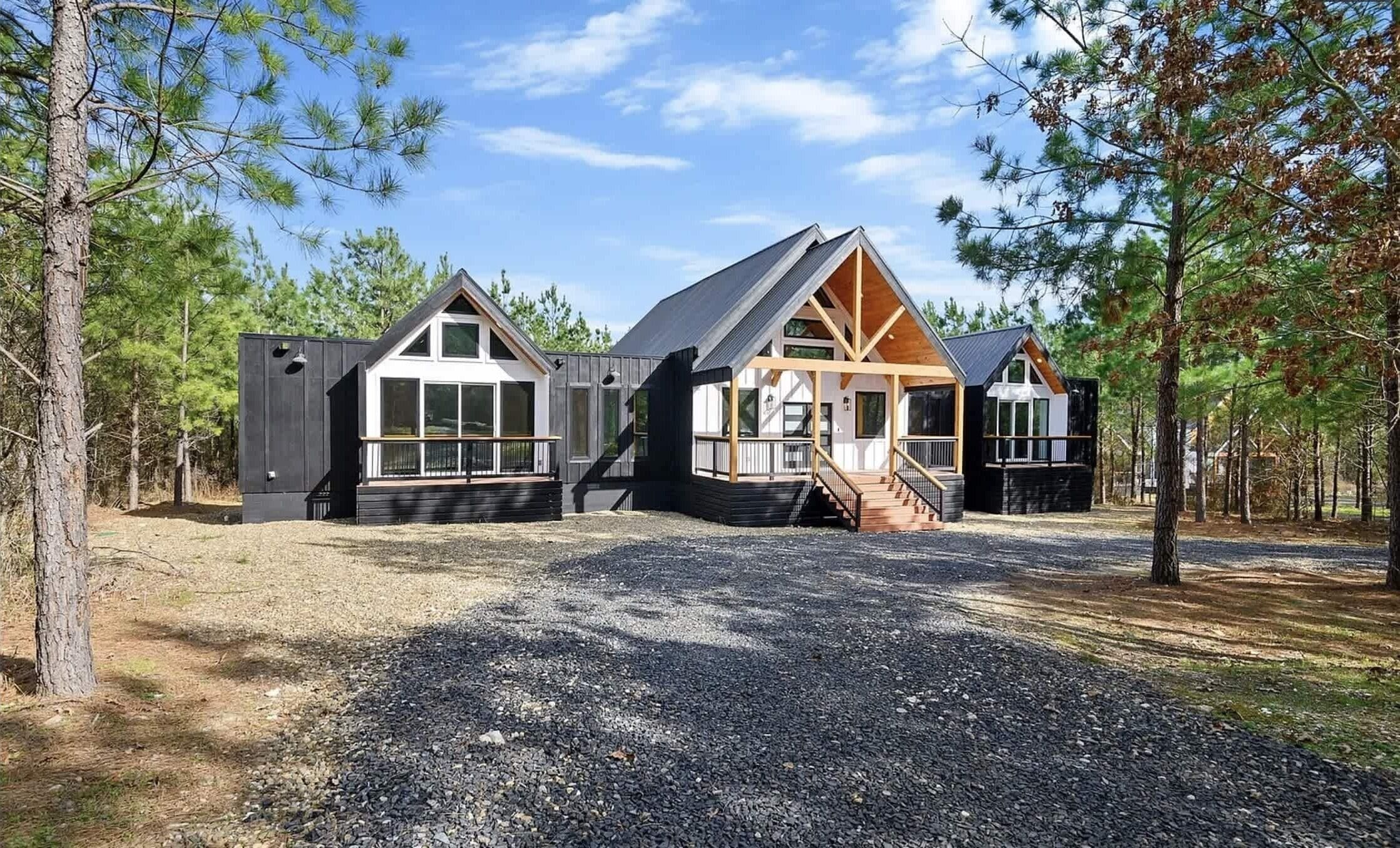 A cabin with a large porch, a staircase, and a gravel driveway.