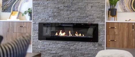 A modern living room with a stone fireplace, wooden cabinets, and a flat-screen TV mounted above the fireplace.