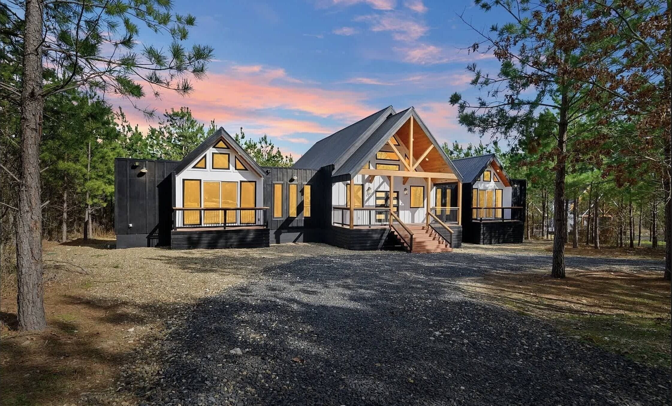 A cabin with a central wooden structure and two attached wings, surrounded by trees.