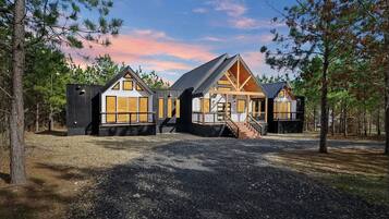 A cabin with a central wooden structure and two attached wings, surrounded by trees.