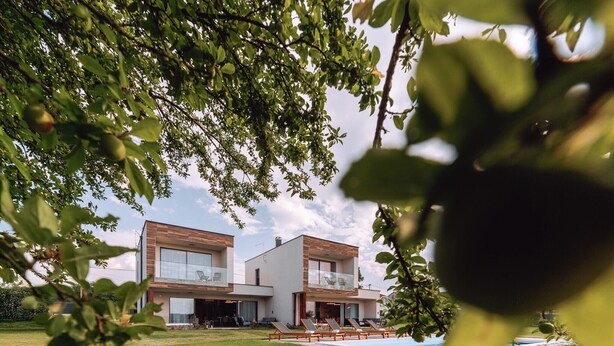 Een modern huis met twee verdiepingen, met een zwembad, omringd door groen.