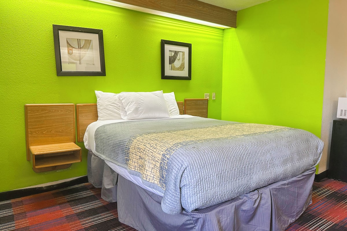 A hotel room with a bed, green walls, two framed pictures, and a wooden nightstand.