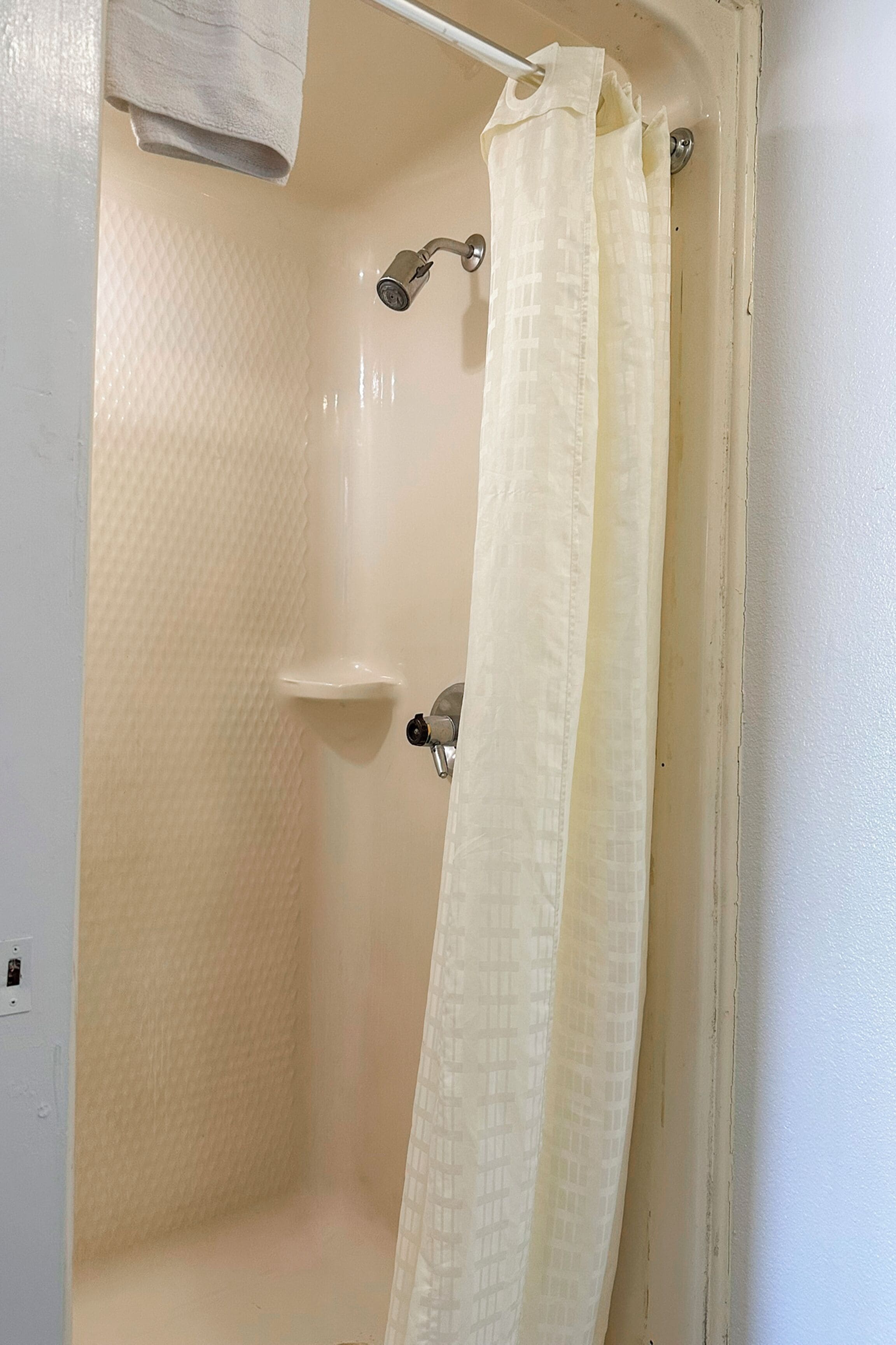 A shower with a beige textured wall, a white towel hanging, and a beige shower curtain.