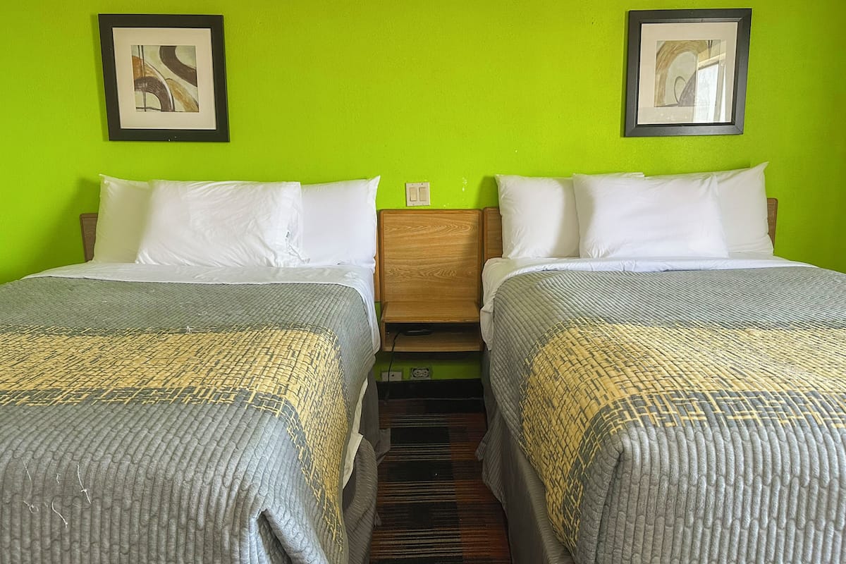 A hotel room with two single beds, green walls, and framed artwork on the walls.