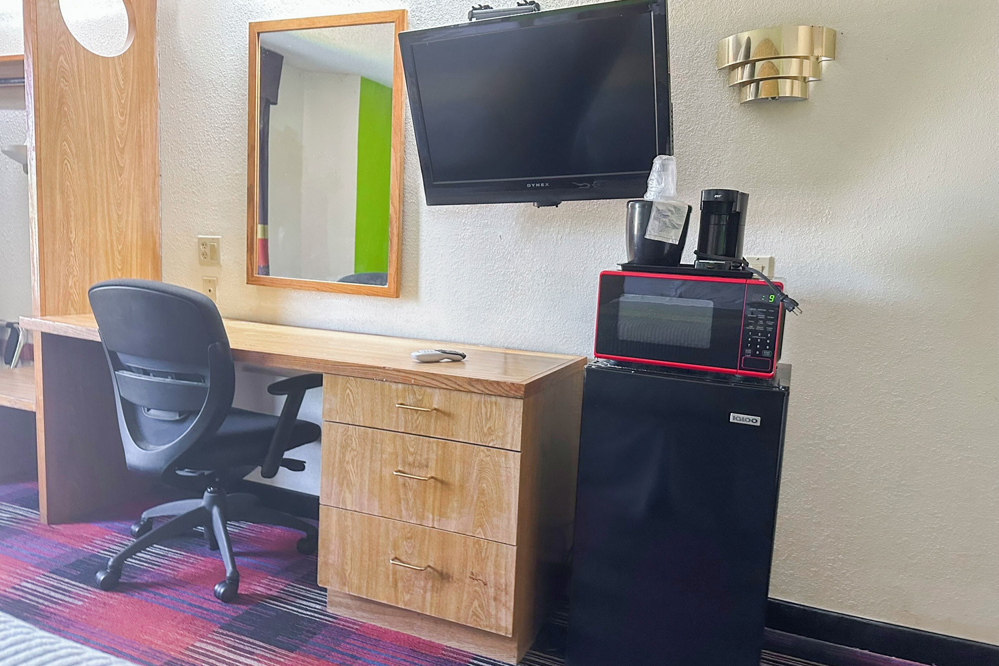 A hotel room with a wooden desk, a black office chair, a television, and a microwave.