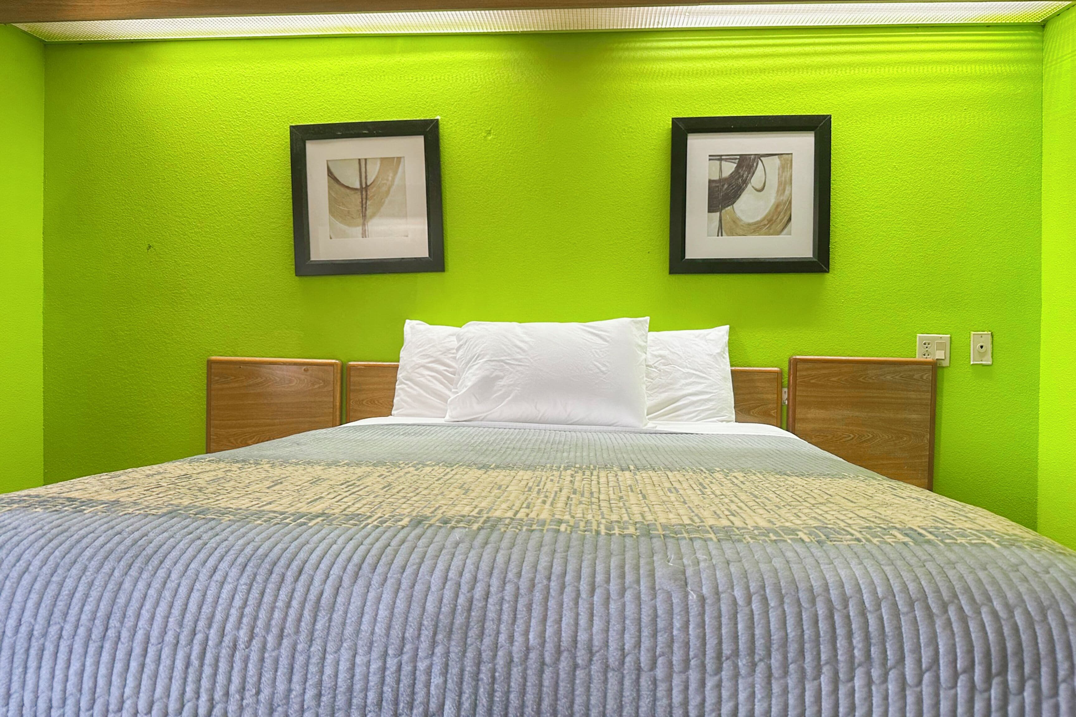 Une chambre d’hôtel avec un lit, des murs verts et deux tableaux encadrés accrochés au mur.