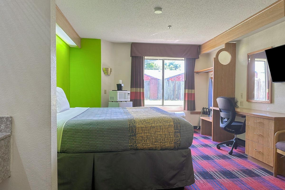 A hotel room with a bed, a desk, a chair, a television, and a window with curtains.