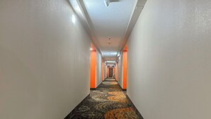 A hotel hallway with a patterned carpet, white walls, and orange accents. - Classic Inn By Townhouse American Way Memphis I 240 (Memphis)