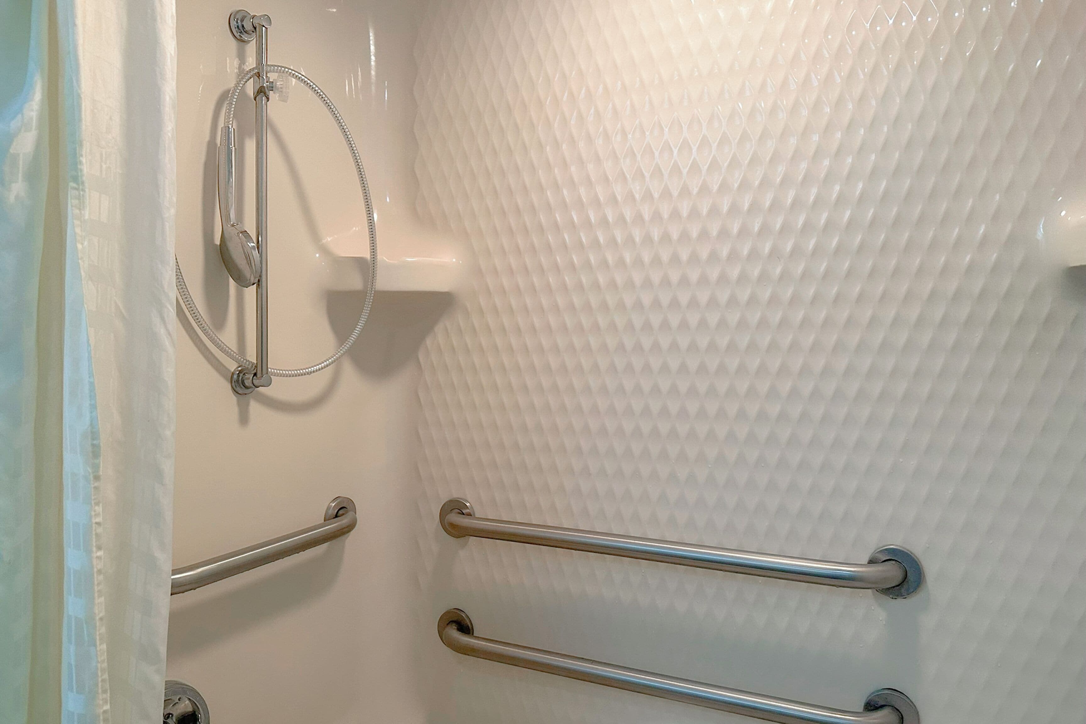 A bathroom with a textured wall, a shower with a handheld showerhead, and two grab bars.