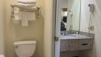 A bathroom with a toilet, a towel rack with folded towels, a sink with a mirror, and a hairdryer on the wall.