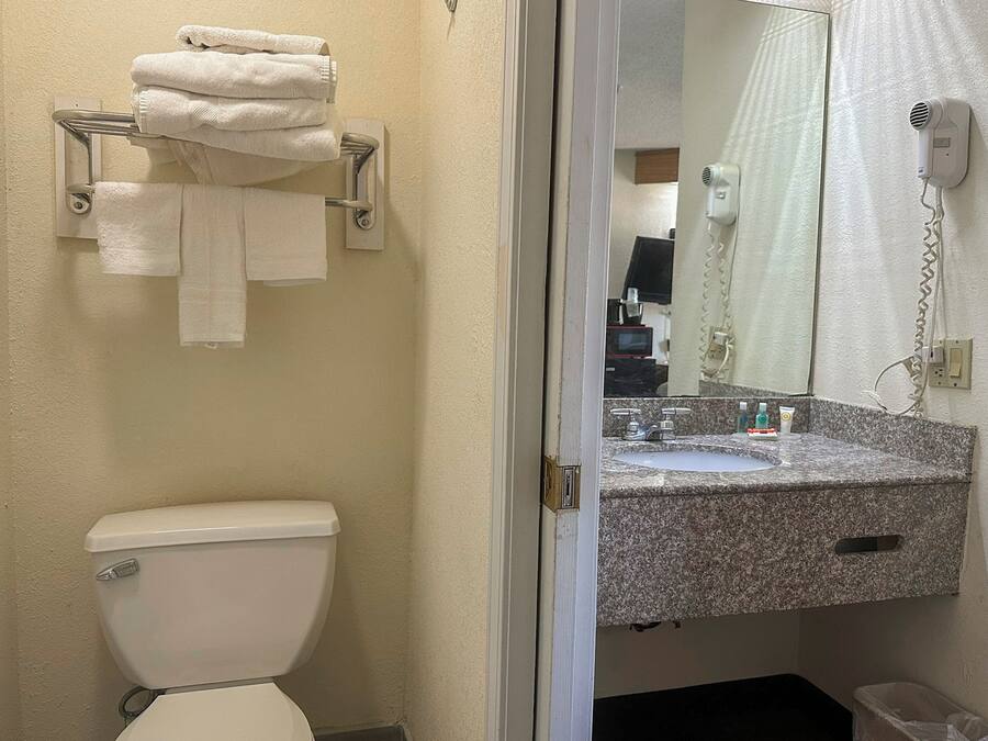 A bathroom with a toilet, a towel rack with folded towels, a sink with a mirror, and a hairdryer on the wall.