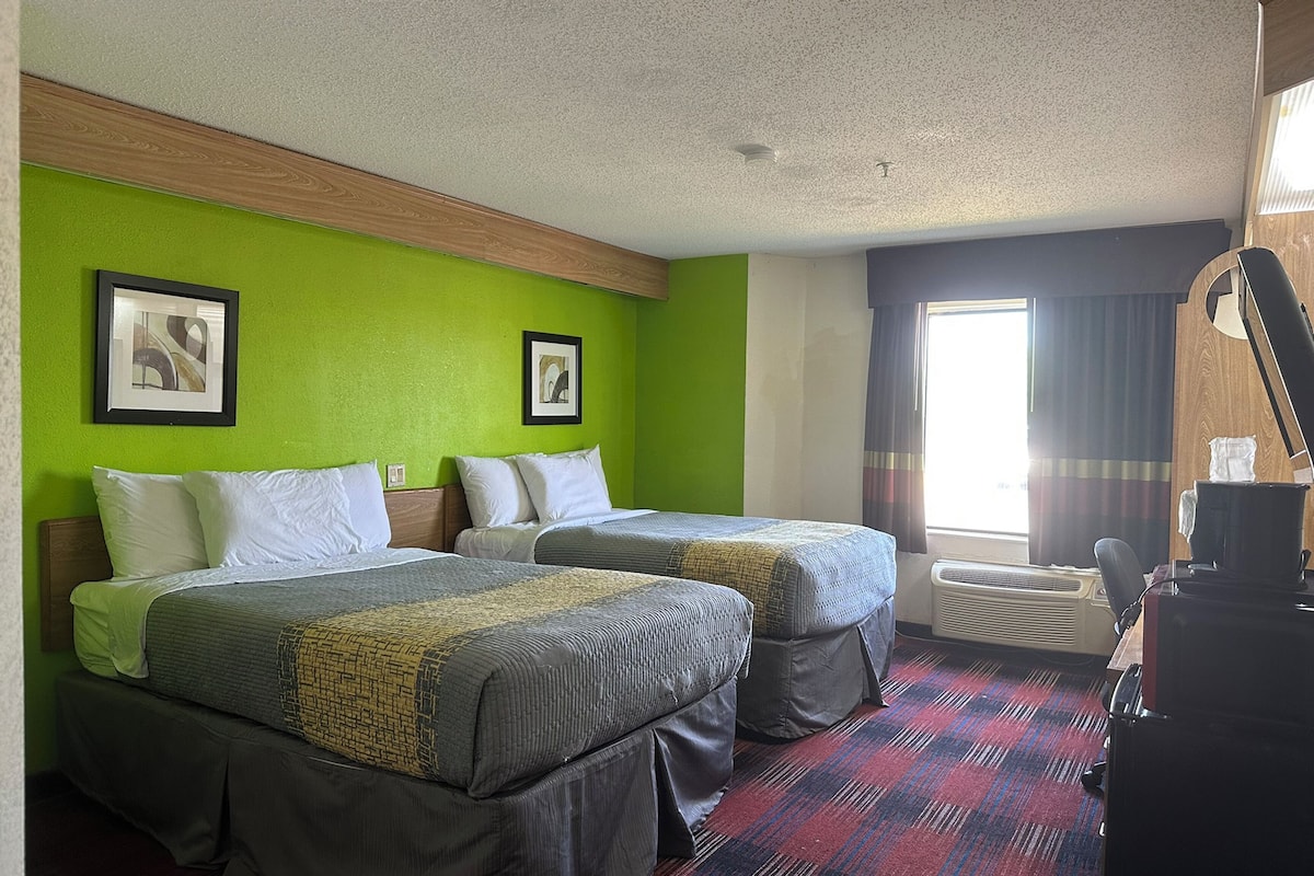 A hotel room with two beds, a desk, and a window with curtains.