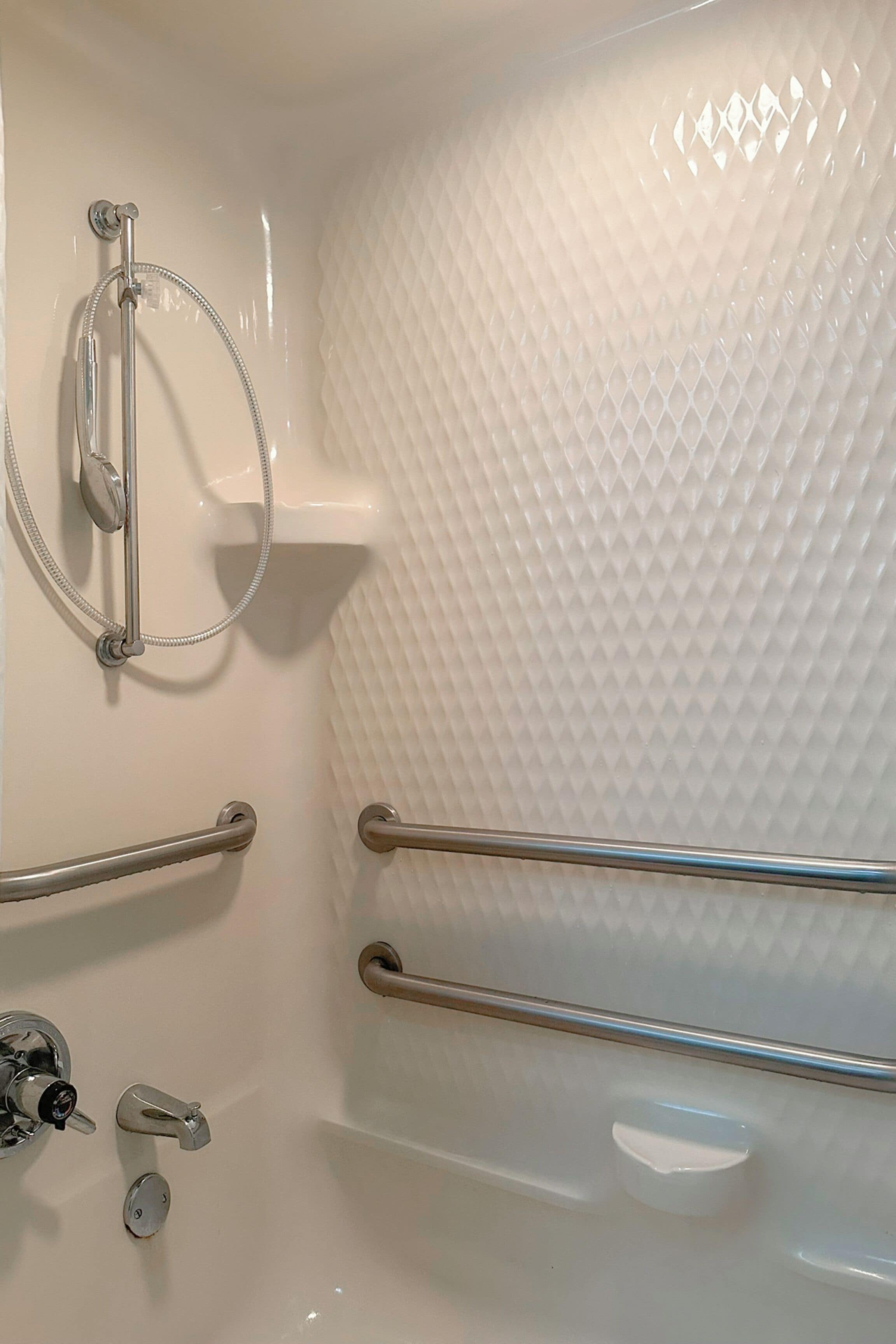 Een witte badkuip met een gestructureerde wand, een handdouche en twee handgrepen.