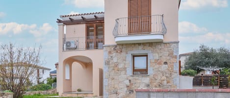 Un bâtiment à deux étages avec une façade en pierre, un balcon doté de volets en bois et une petite fenêtre.