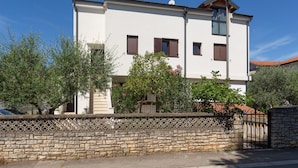 A two-story building with a stone wall in front, a tiled roof, and a gate.