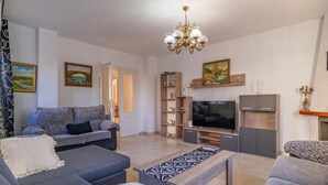Una sala de estar con un sofá, una mesa de centro, un televisor y una estantería.