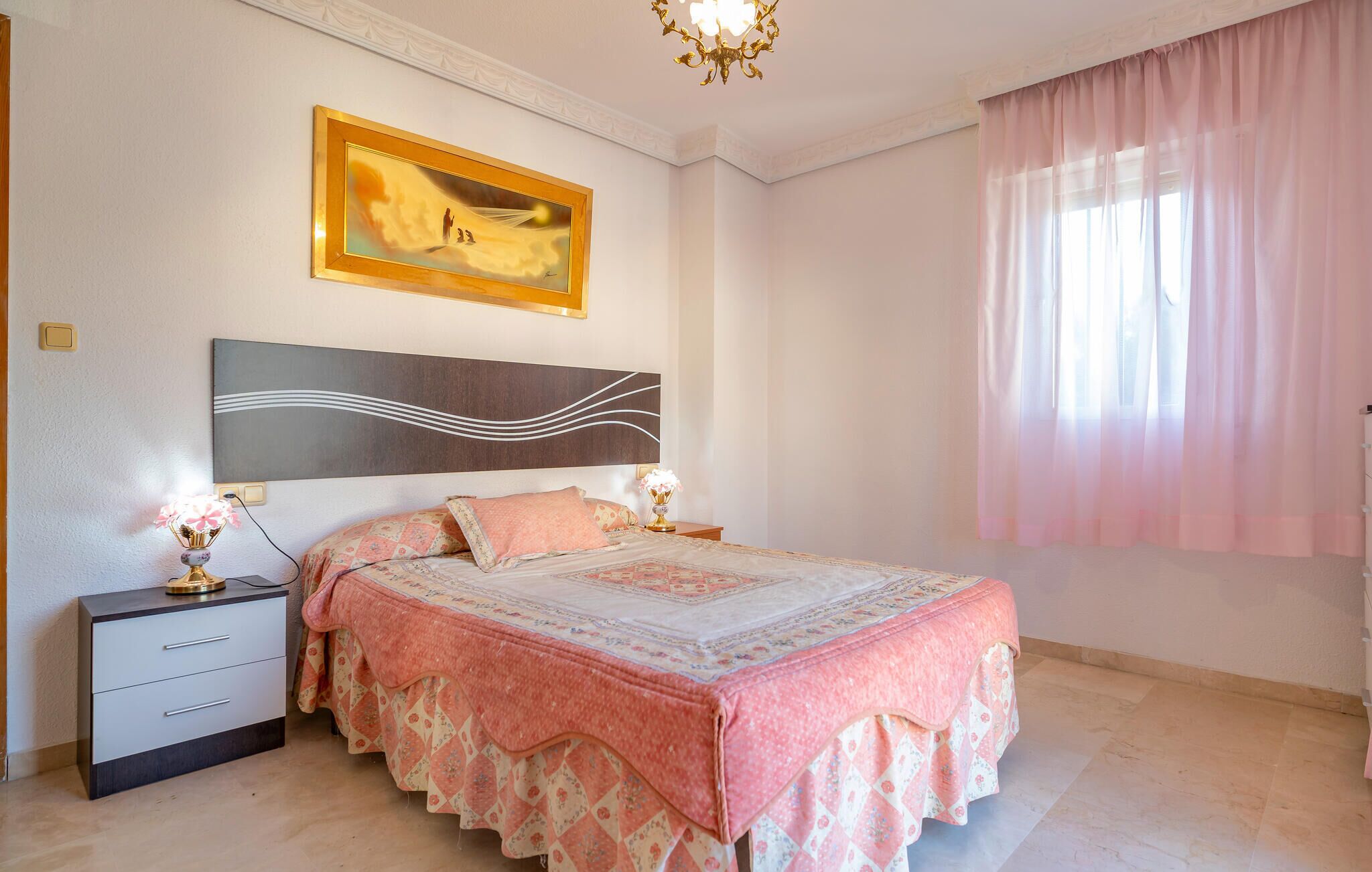 A bedroom with a bed, nightstands, a lamp, a painting, and a window with curtains.