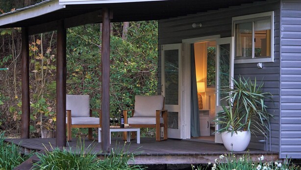 A wooden deck with two chairs and a table, surrounded by greenery. - Kick back in a calm, stylish space in the foothills of the Watagan Mountains (Cooranbong)