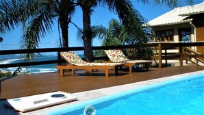 A pool area with lounge chairs and a wooden deck overlooking the ocean. - Casa Vista Privilegiada - Piscina e Mar (Garopaba)