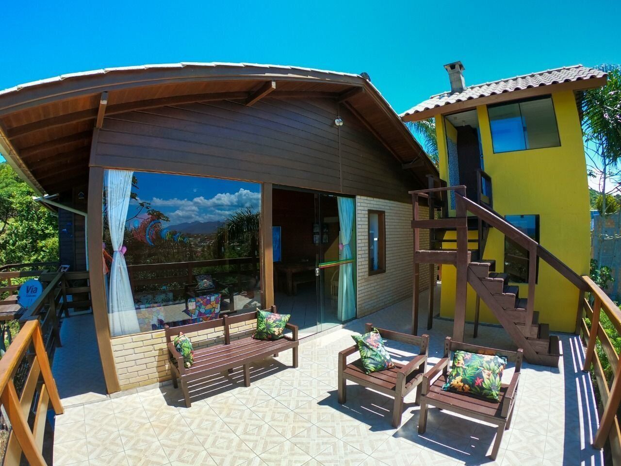 A two-story building with a covered patio area featuring wooden furniture and a staircase.