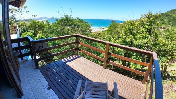 A wooden deck with a railing overlooking a beach and greenery. - Casa Vista Privilegiada - Piscina e Mar (Garopaba)