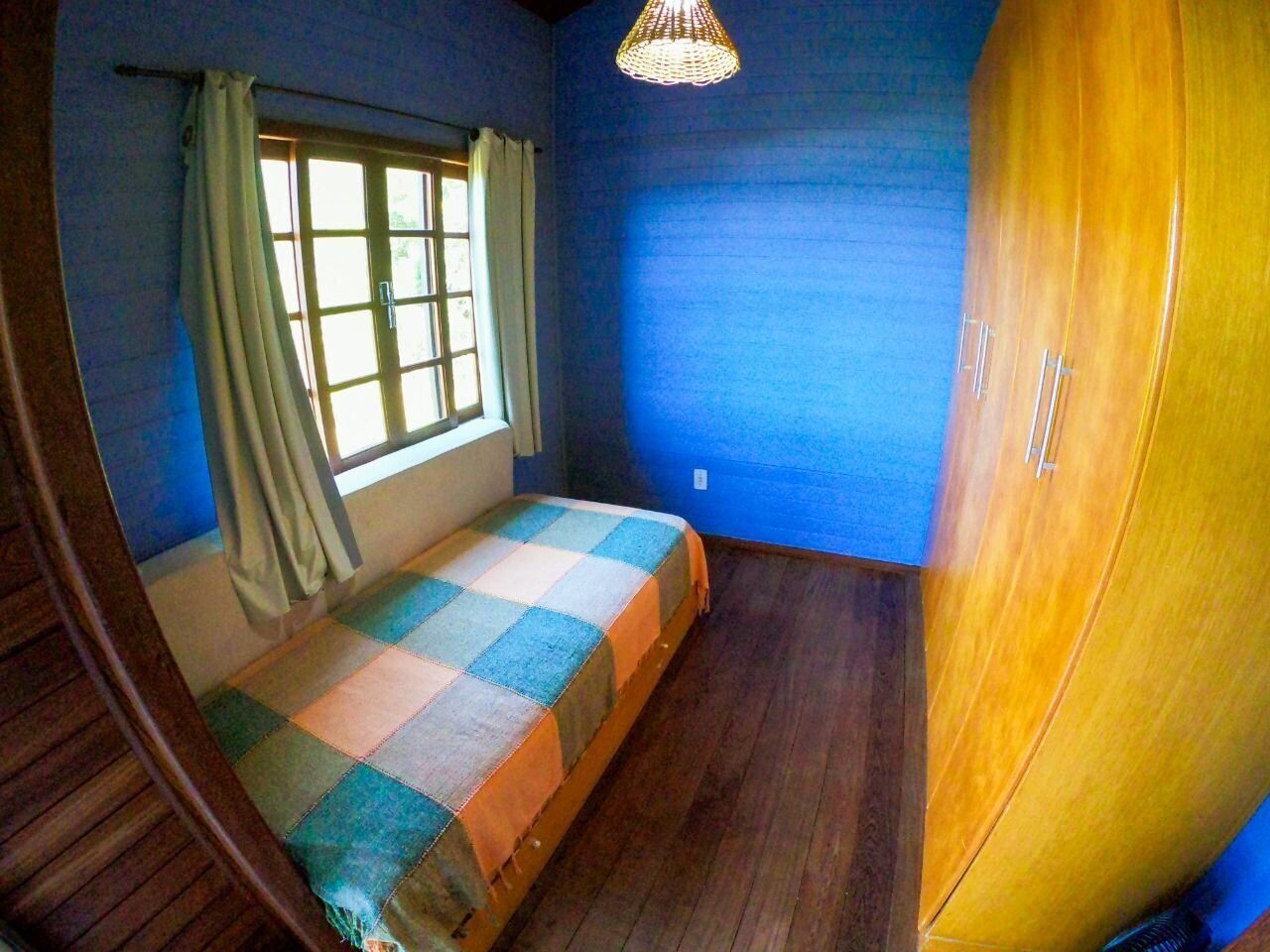 A room with a bed, a window with curtains, a wooden wardrobe, and a hanging light fixture.