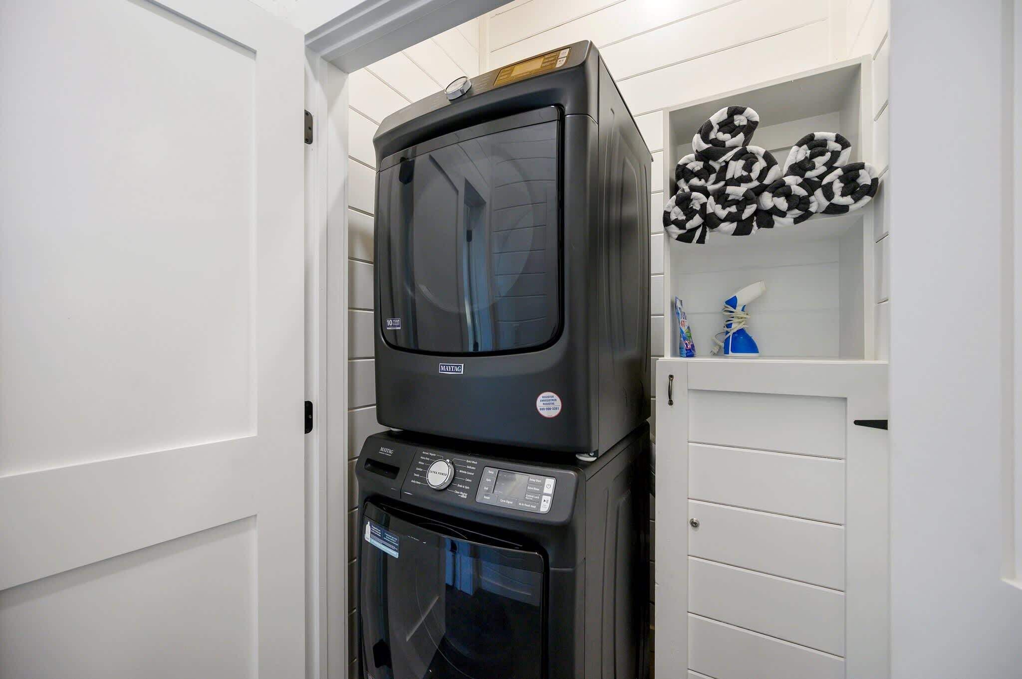 A compact kitchen with a microwave and oven stacked on top of each other, a white cabinet with a black and white patterned towel, and a small shelf with toiletries.