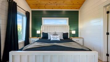 A bedroom with a wooden ceiling, a large window, a bed with a headboard, two bedside tables with lamps, and a green accent wall.