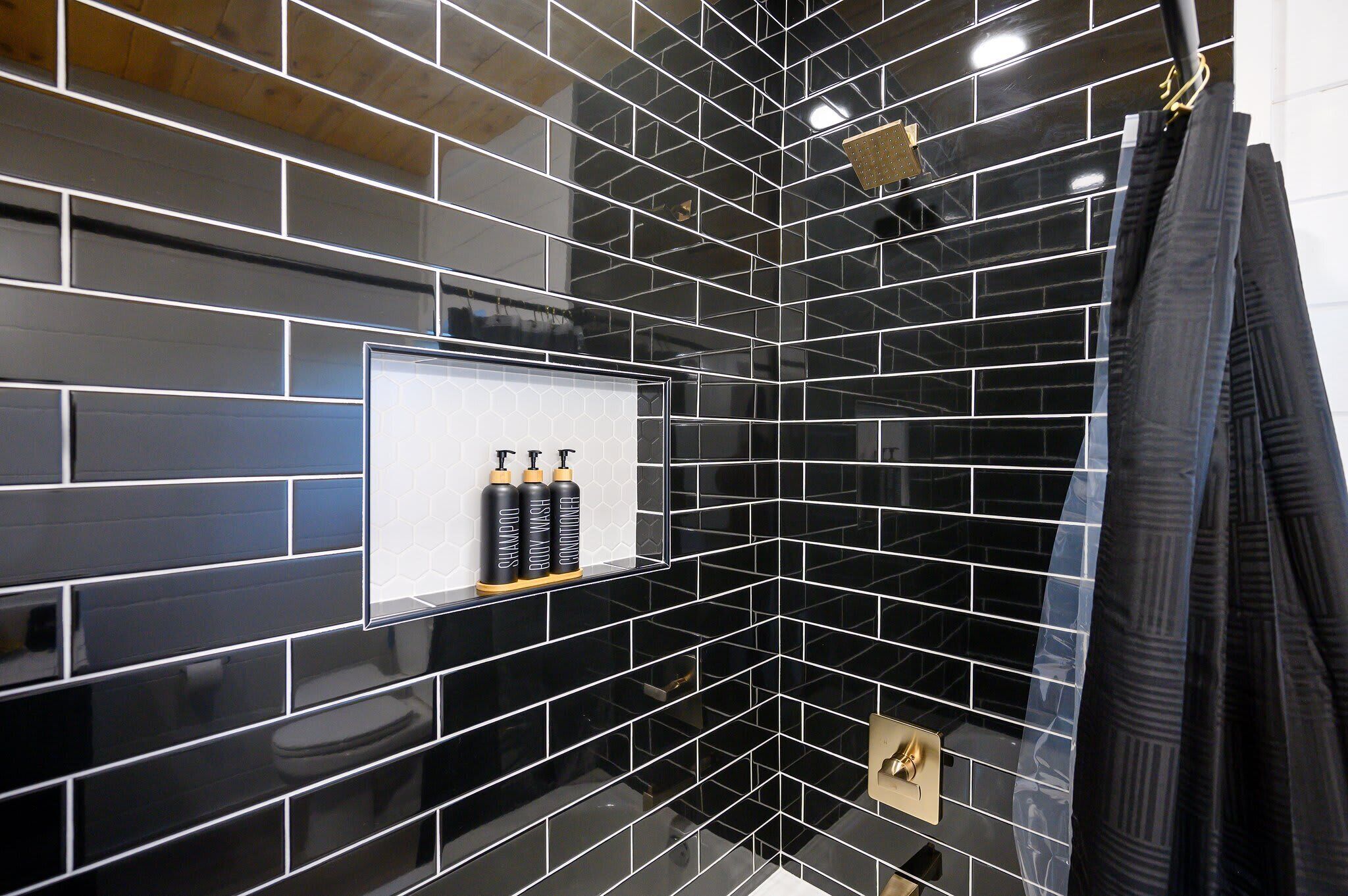 Une salle de bain avec des carreaux noirs brillants, un tableau encadré représentant des articles de toilette et un robinet doré.