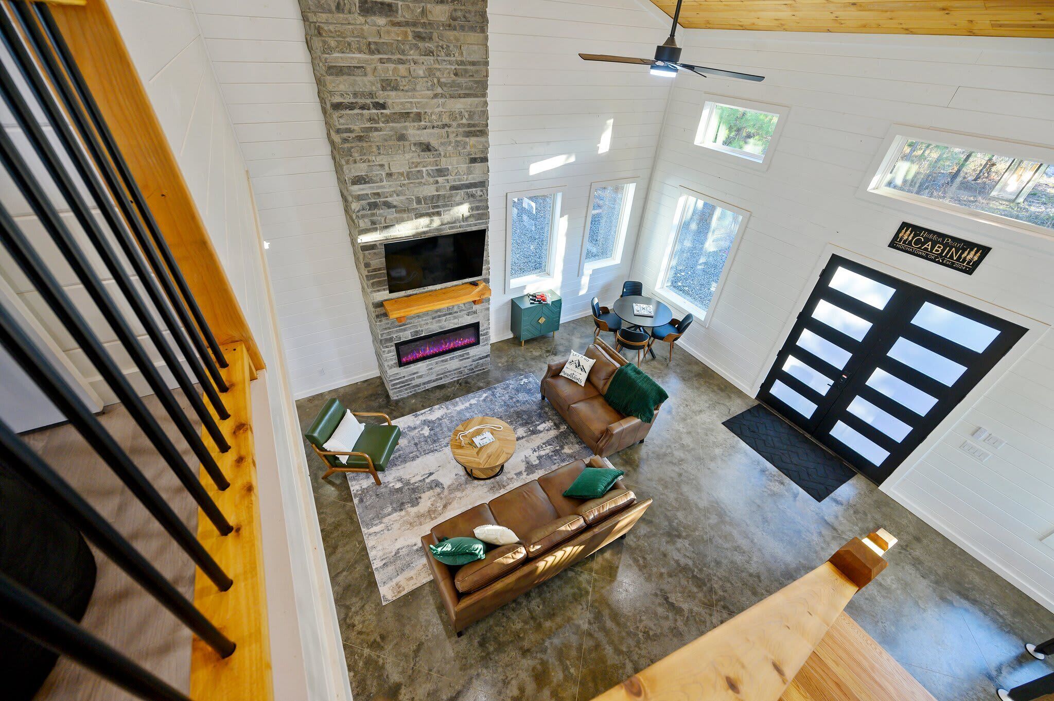 A spacious living area with a stone fireplace, a sofa, and a coffee table. There are large windows and a ceiling fan.