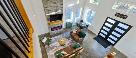 A spacious living area with a stone fireplace, a sofa, and a coffee table. There are large windows and a ceiling fan.