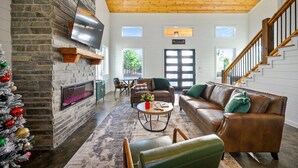 A cozy living room with a stone fireplace, leather sofas, a flat-screen TV, and a Christmas tree. - New, Modern, Bunk Room, Game Room, Playground, Hot tub (Broken Bow)