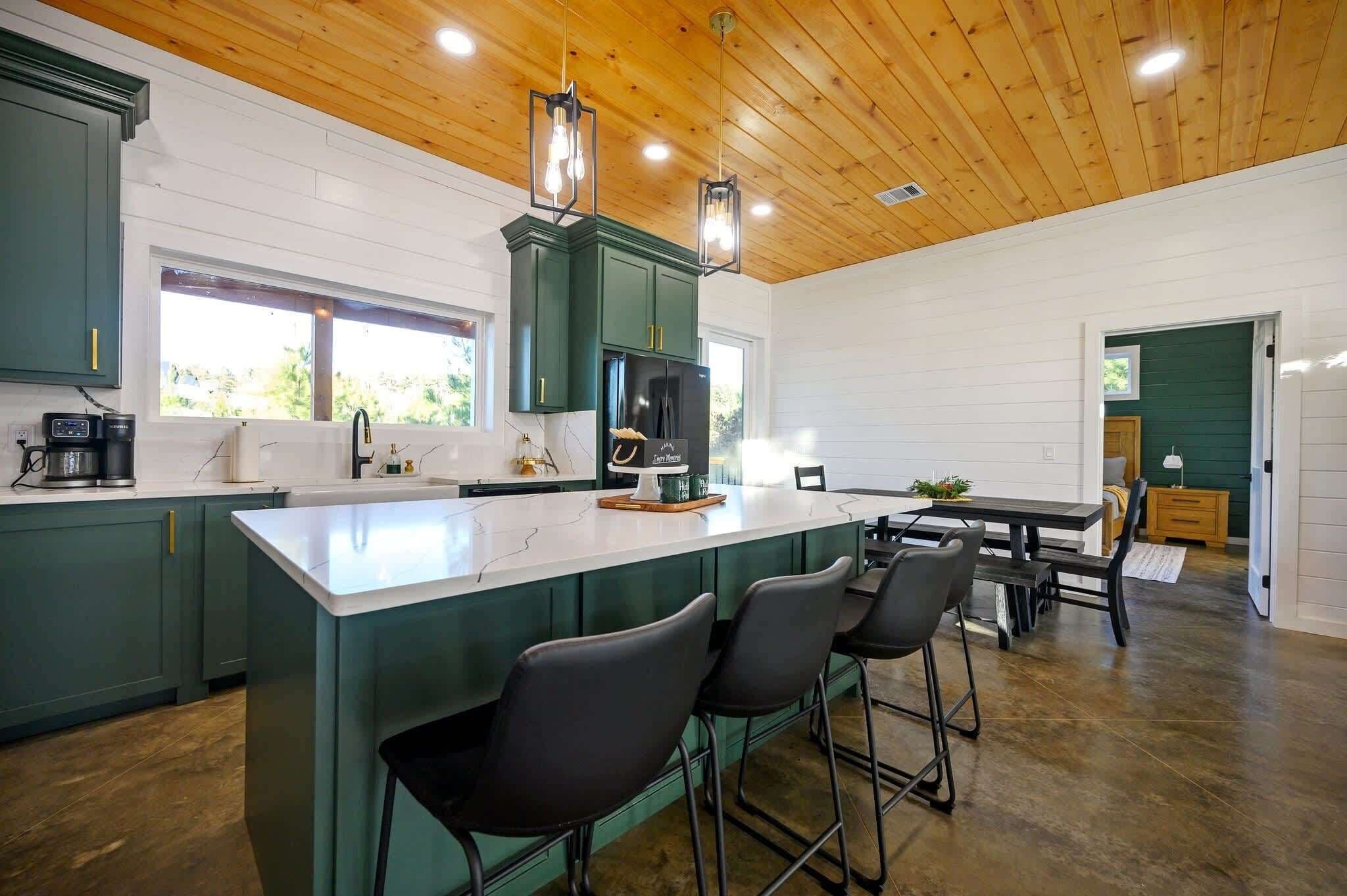 Uma cozinha moderna com uma ilha central, banquetas de bar e uma área de jantar com mesa e cadeiras.