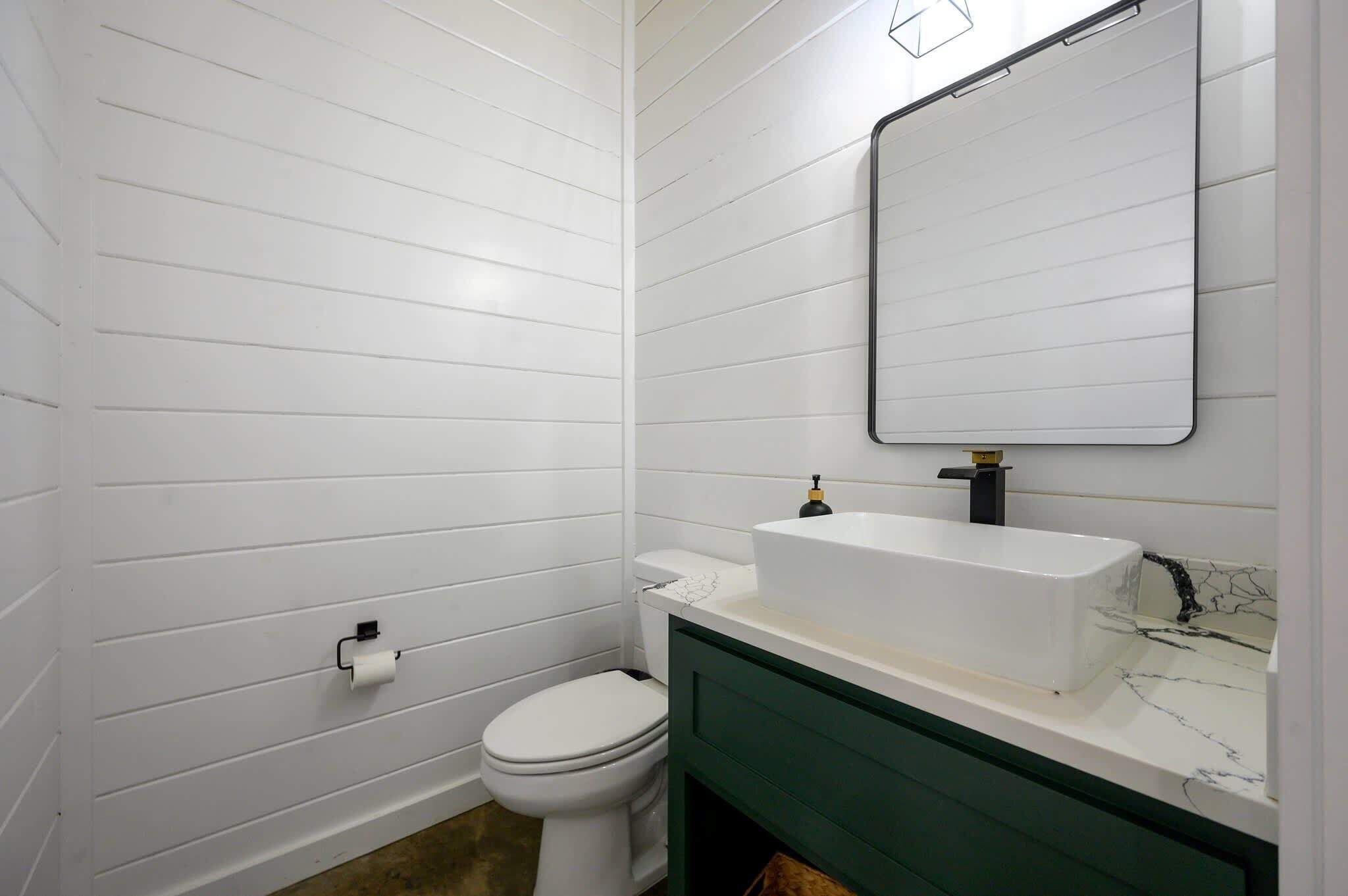 A bathroom with white paneled walls, a white toilet, a white sink with a black faucet, and a green vanity.