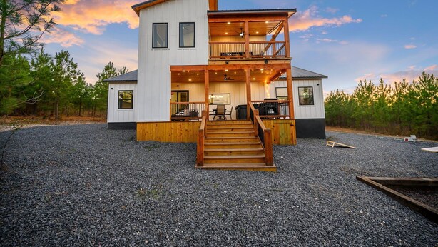 A modern two-story house with a wooden staircase leading to a balcony. - New, Modern, Bunk Room, Game Room, Playground, Hot tub (Broken Bow)