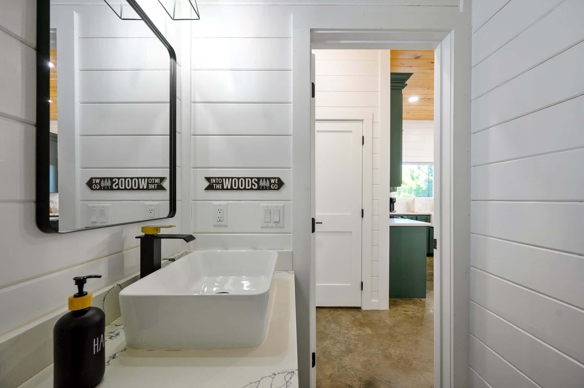 A modern bathroom with a large white sink, a mirror, and a black soap dispenser.