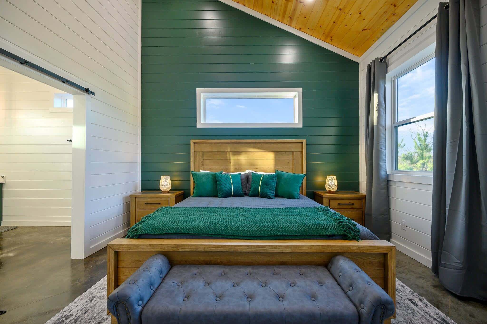 A bedroom with a wooden bed, green walls, a skylight, and a view of the outdoors.