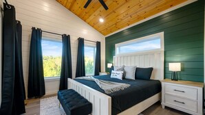 A bedroom with a bed, nightstand, bench, and a view of greenery outside. - New, Modern, Bunk Room, Game Room, Playground, Hot tub (Broken Bow)