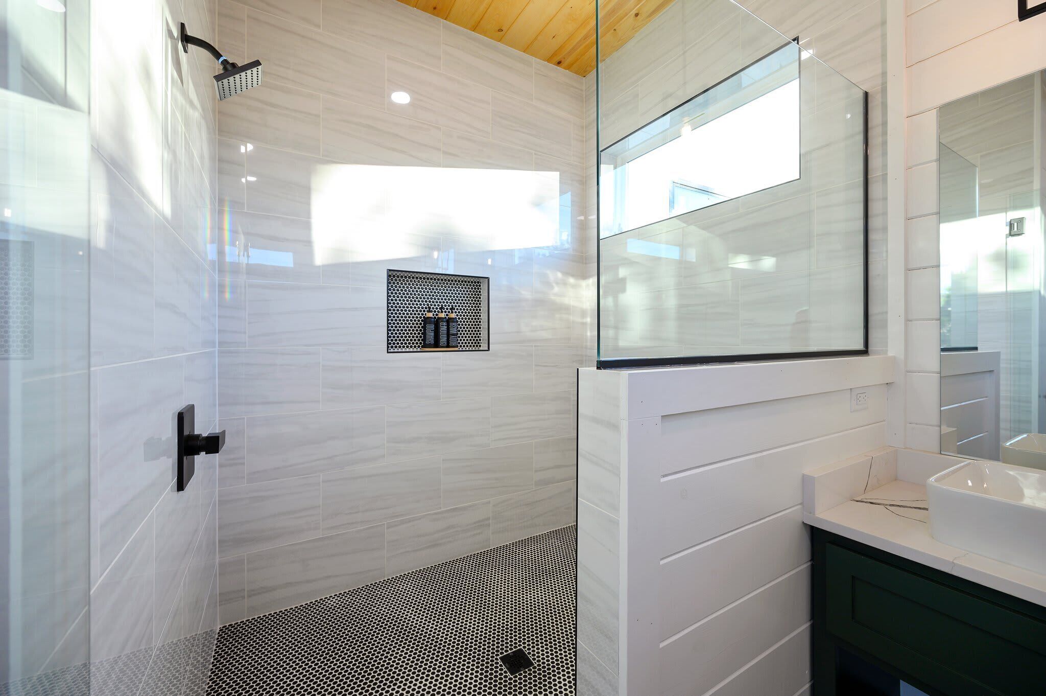 Une salle de bain moderne avec une douche à l’italienne en verre, un grand miroir et un lavabo blanc.