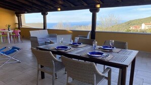 Un área de comedor al aire libre con una mesa preparada para cuatro personas, rodeada de sillas de mimbre y vistas del paisaje.