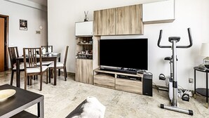 A living room with a TV, exercise bike, dining area, and built-in shelves.