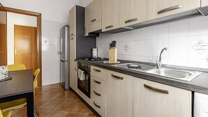 A modern kitchen with light wood cabinets, a stainless steel sink, and a built-in oven.