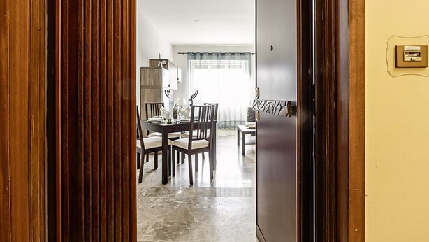 A room with a dining table and chairs, a sofa, and a wooden door.