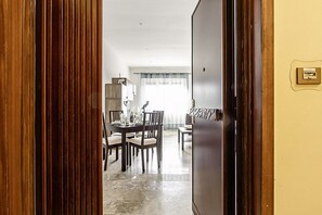 A room with a dining table and chairs, a sofa, and a wooden door. - Gran Rivadavia by Rentbeat (Roma)