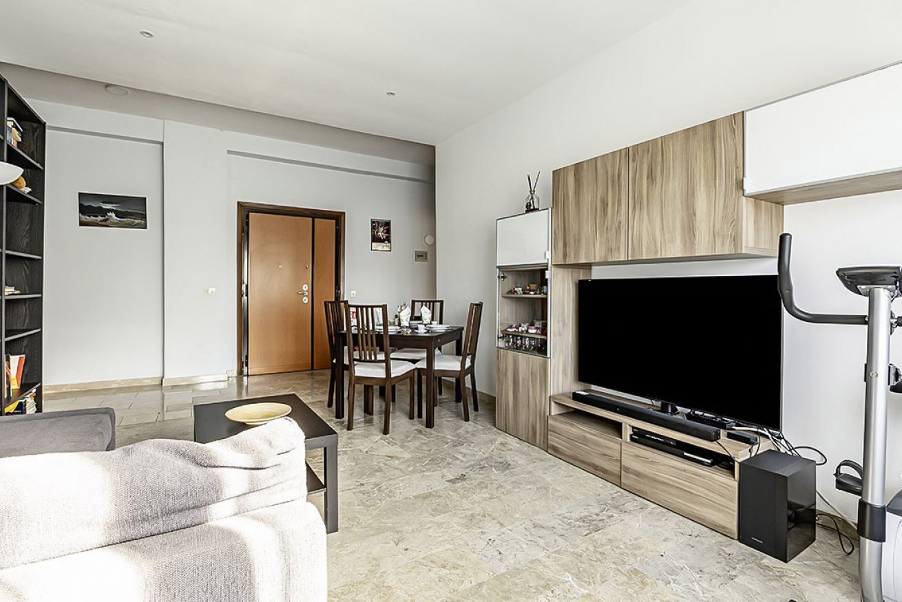 A modern living room with a dining area, a flat-screen TV, and a workout machine.