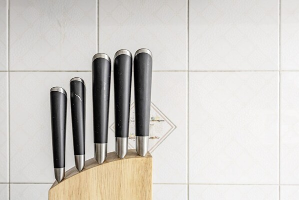 A set of knives with black handles and silver blades, arranged on a wooden block against a tiled wall. - Gran Rivadavia by Rentbeat (Roma)